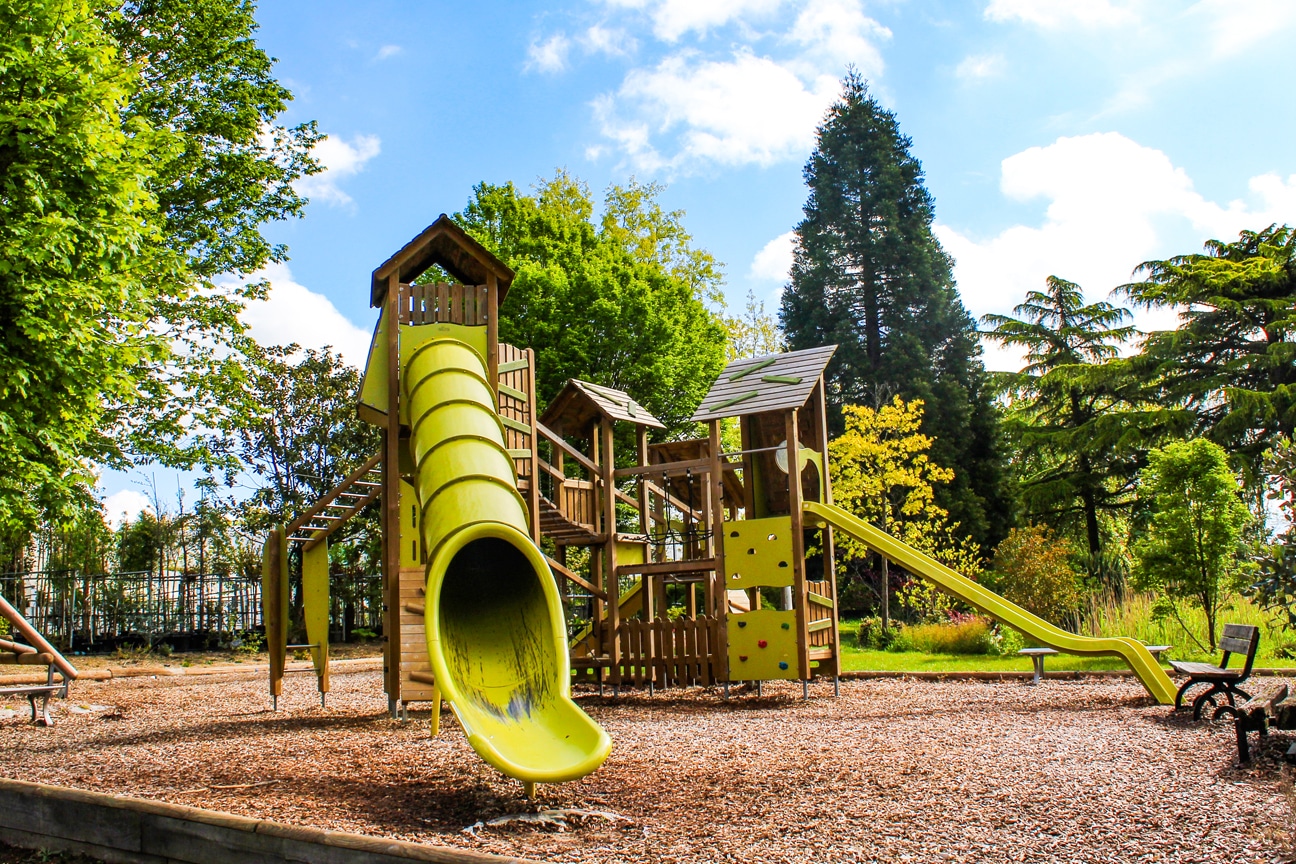 Aire de jeux extérieure ensoleillée avec toboggans et arbres.